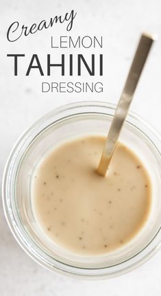 a spoon sticking out of a jar filled with tahini dressing on a white surface