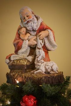 a statue of santa claus holding a baby in his lap next to a christmas tree