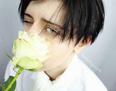 a woman with black hair holding a white rose in her mouth and looking at the camera