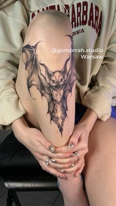 a woman sitting on top of a chair with a bat tattoo on her arm