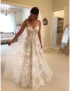 a woman wearing a wedding dress with flowers on the skirt and veil, standing in a room