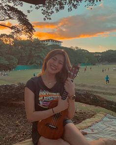 a woman sitting on a blanket holding an ukulele in her hand and smiling