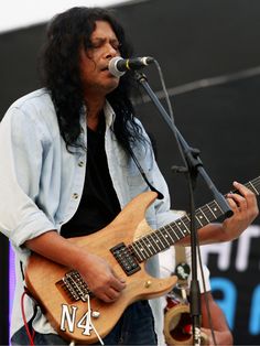 a man with long hair playing an electric guitar in front of a microphone on stage