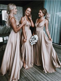 three beautiful women standing next to each other in long dresses and one is holding a bouquet