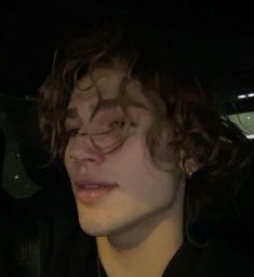 a young man with curly hair sitting in the back seat of a car at night