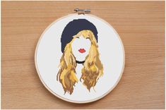 a cross - stitch portrait of a woman wearing a beanie on a wooden surface