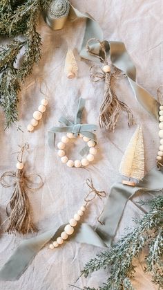 christmas decorations and ribbons laid out on a white tablecloth with silver bells, pine cones, and other ornaments