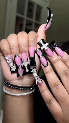 a woman's hands with pink and black nail polishes on their nails, holding a cross bracelet