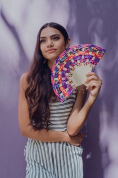 a woman is holding a colorful fan in front of a purple wall and posing for the camera