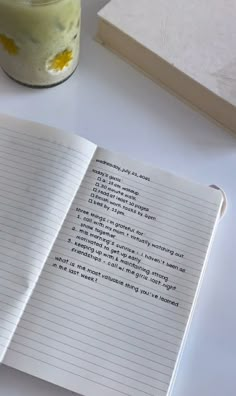 an open notebook sitting on top of a table next to a jar of paint and a pen