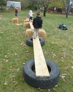 two children are playing in the yard with large tires and hay bales on the grass