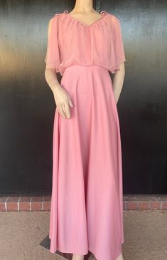 1970s maxi dress. Pink polyester. Polyester chiffon bodice overlay. Decorative bows on shoulders. Nylon zip back. Measurements 36" bust 26" waist 16" bodice length  58" length 44" hips Lovely dress shows well, with no obvious damage or wear. Pink Empire Waist Maxi Dress For Bridesmaid, Pink Chiffon Maxi Dress For Prom Season, Flowy Pink Maxi Dress For Evening, Pink Empire Waist Maxi Dress For Evening, Pink Chiffon Evening Maxi Dress, Vintage Pink Chiffon Dress, Pink Ruffled Maxi Dress For Formal Occasions, Pink Chiffon Cocktail Maxi Dress, Pink Full Length Maxi Dress For Spring