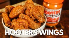 a white bowl filled with fried wings next to a jar of hot sauce