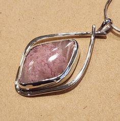 I created this abstract design to highlight the beauty of this Pink Rhodochrosite stone in a way to accent its natural character. This Sterling Silver Pendant is about 1-1/2 inches long and 7/8 inches wide. It has a 22 mm x 14 mm freeform parallelogram shaped and cut Rhodochrosite natural stone.   A freind of mine cut shaped and polished this stone for me.  I am including a 18 inch Sterling Silver mm 8 sided Snake Chain so your pendant can be worn right away. Modern Pink Gemstone Jewelry, Pink Necklace With Large Pendant, Artisan Pink Gemstone Jewelry, Unique Pink Necklace With Large Pendant, Handmade Elegant Pink Opal Jewelry, Elegant Handmade Pink Opal Jewelry, Pink Agate Pendant Jewelry, Pink Natural Stones Gemstones In Sterling Silver, Silver Rhodonite Jewelry With Natural Stones