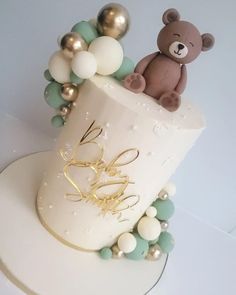 a teddy bear sitting on top of a white cake with balloons and beads around it