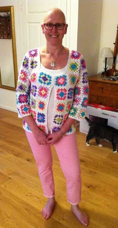 a woman standing in front of a mirror wearing pink pants and a crocheted sweater