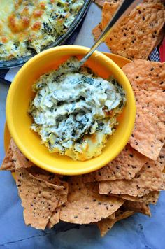 a yellow bowl filled with spinach dip surrounded by tortilla chips and crackers