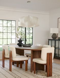 a dining room table with four chairs and a vase on top of it in front of a large window