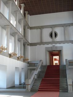 an empty building with stairs leading up to the door and red carpet on the floor