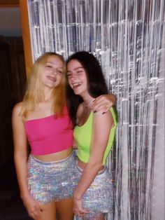 two young women standing next to each other in front of a wall covered with tinsel