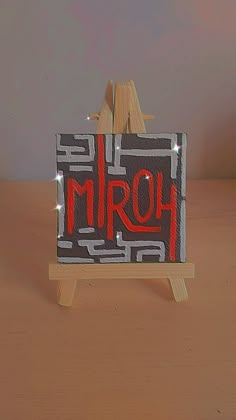 a small wooden easel holding an art piece with the word mrq on it