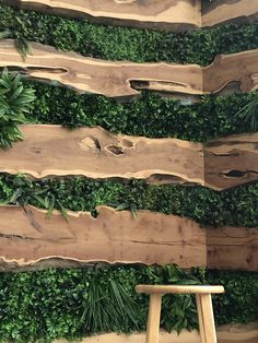 a wooden stool sitting in front of a wall covered with green plants and wood planks