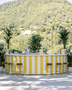 an outdoor bar with yellow and white stripes on the counter, surrounded by potted plants