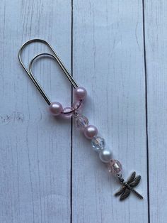 a pair of earrings with charms attached to them on a white wooden surface and a dragonfly charm hanging from the hook