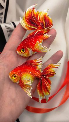 two red and yellow fish sitting on top of a persons hand next to each other