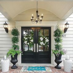 two large black vases with white flowers are on the front porch