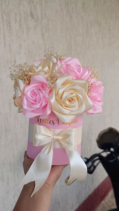 a hand holding a pink and white box with flowers in it on a bike handle