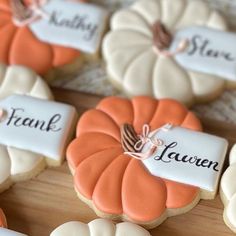 decorated cookies with name tags on them sitting on a wooden table next to white and orange pumpkins