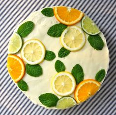 a cake decorated with lemons, oranges and mint leaves on a blue striped tablecloth