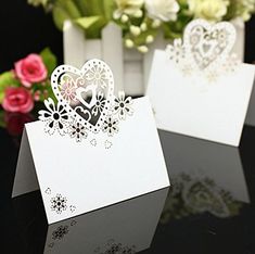 two white cards with hearts on them sitting next to some pink and white flowers in a vase