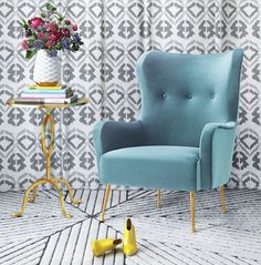 a green chair sitting on top of a wooden floor next to a vase filled with flowers