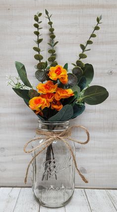 a mason jar filled with orange flowers and greenery