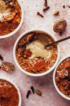 three bowls filled with pudding and nuts on top of a white tablecloth covered in powdered sugar