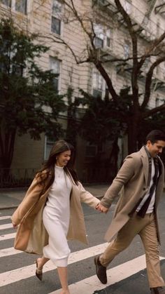 a man and woman walking across a crosswalk holding each other's hands in the city