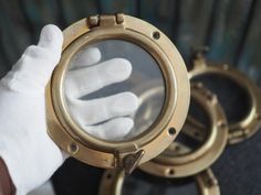 a person in white gloves holding up a brass porthole with two hands on it