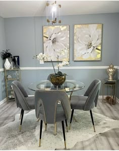 a dining room table with chairs and a vase on top of it in front of two paintings