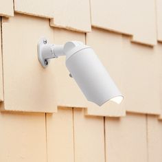 a white light is on the side of a wall next to a tan building with brown shingles