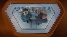 two men looking at each other through a window in a space station, from above