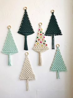 four crocheted christmas trees hanging from hooks on a white wall with beaded details