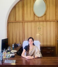 a woman sitting at a desk in front of a wooden paneled wall with an arched window