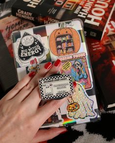 a woman's hand with red nail polish holding onto a small case filled with stickers