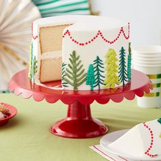 a white cake with pine trees on it sitting on a red plate next to plates