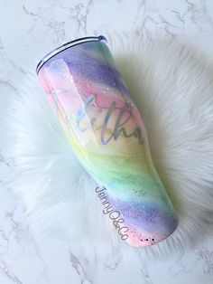 a rainbow colored tumbler sitting on top of a white fur covered floor with the word hello written in cursive writing