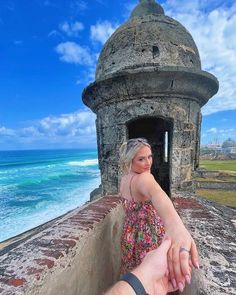 a woman holding the hand of a man in front of an old tower by the ocean