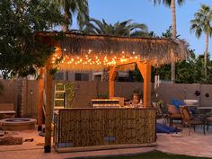 a tiki bar with lights hanging from it's roof and palm trees in the background