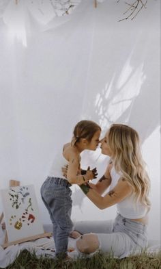 a mother and her child are sitting on the ground in front of an easel